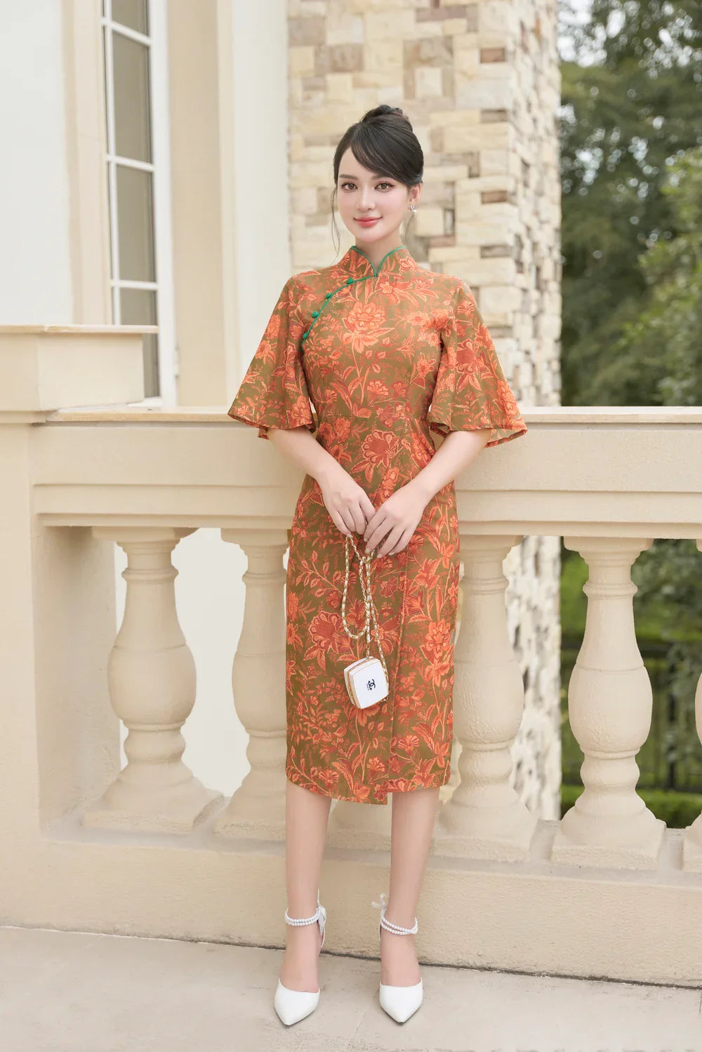 Woman in orange floral modern cheongsam dress with flutter sleeves standing outdoors