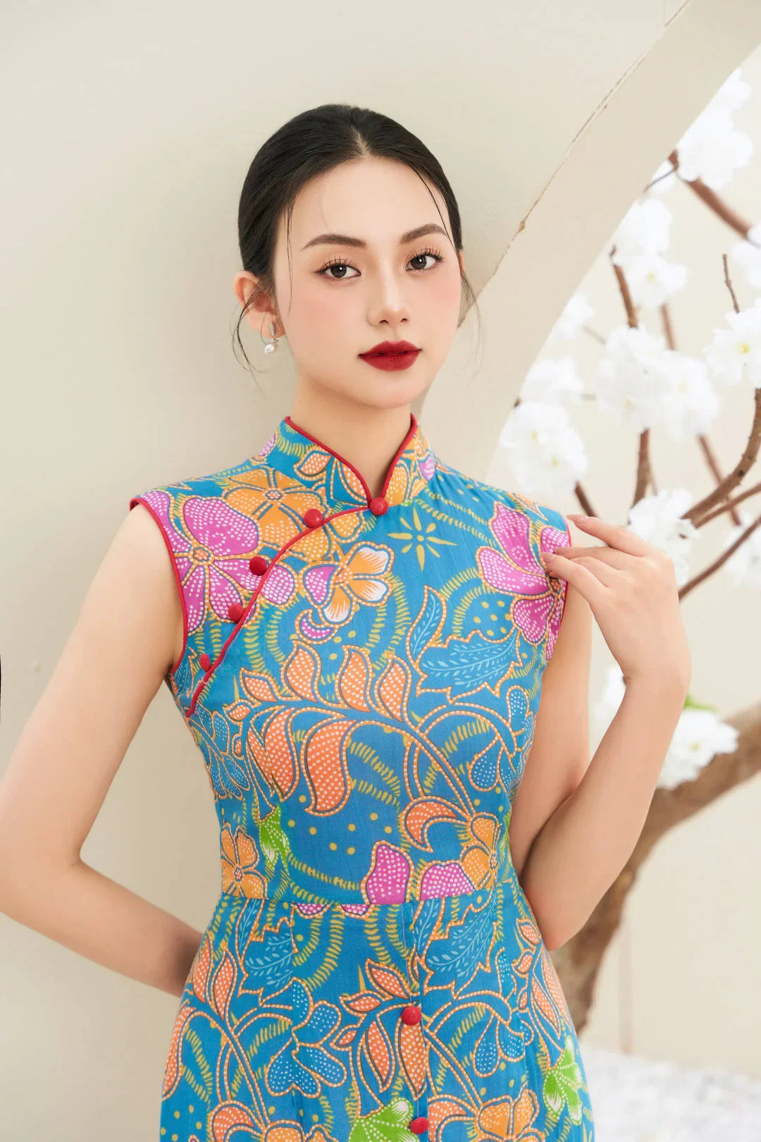 Woman in a modern blue floral cheongsam with mandarin collar standing beside white blossoms