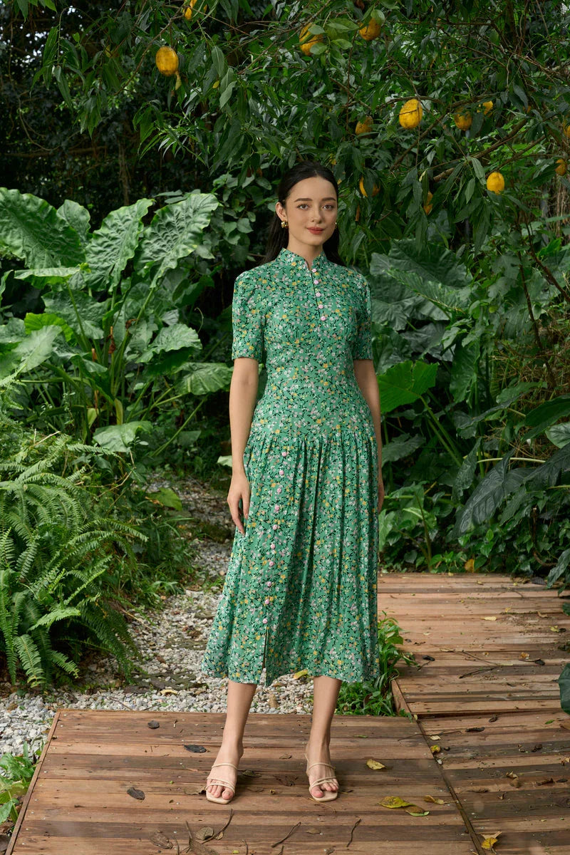 Woman in a green floral cheongsam dress standing on wooden path in lush garden