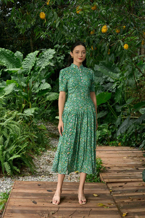 Woman in a green floral cheongsam dress standing on wooden path in lush garden