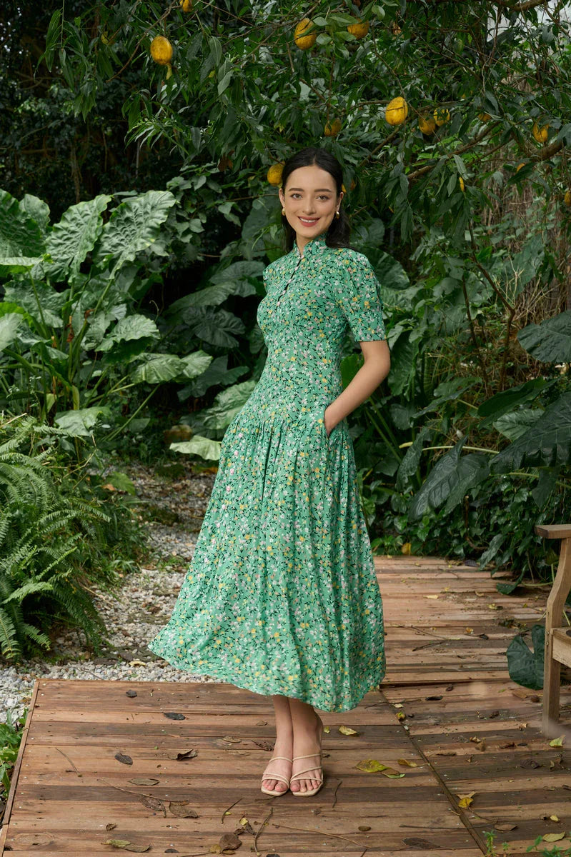 Woman in green floral modern cheongsam dress standing outdoors surrounded by lush plants