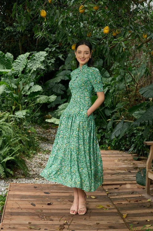 Woman in green floral modern cheongsam dress standing outdoors surrounded by lush plants