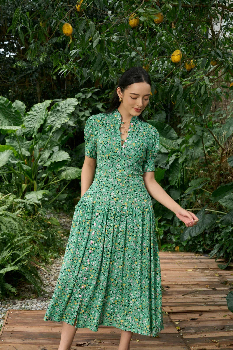 Woman wearing a green floral cheongsam dress with short sleeves, standing in a lush garden