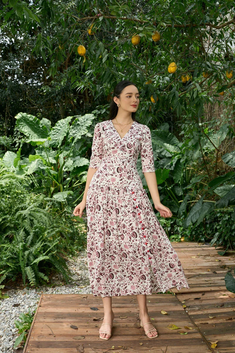 Woman in a floral print midi dress with three-quarter sleeves, standing outdoors on wooden path surrounded by lush greenery.