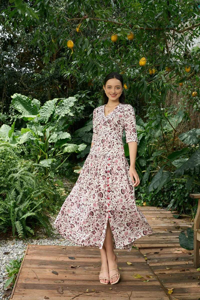 Woman in floral print cheongsam-inspired dress with three-quarter sleeves, standing in a lush garden