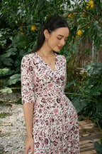 Woman in a white floral print dress with elbow sleeves, standing in a garden