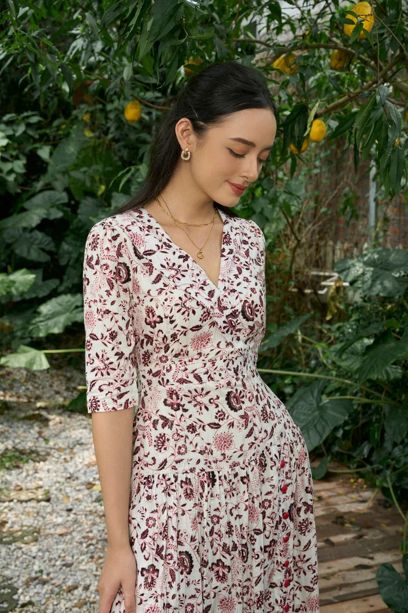 Woman in a white floral print dress with elbow sleeves, standing in a garden