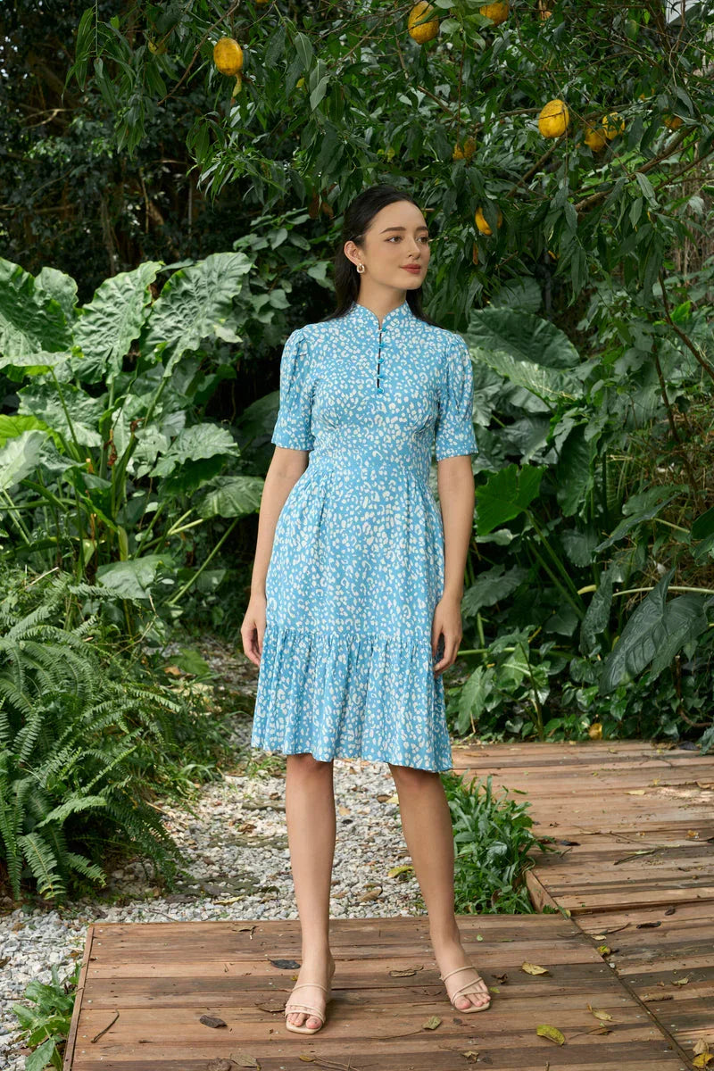 Woman in blue cheongsam-inspired midi dress with white pattern standing outdoors