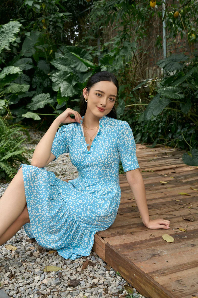 Woman in a blue printed cheongsam-inspired dress sitting on a wooden deck outdoors