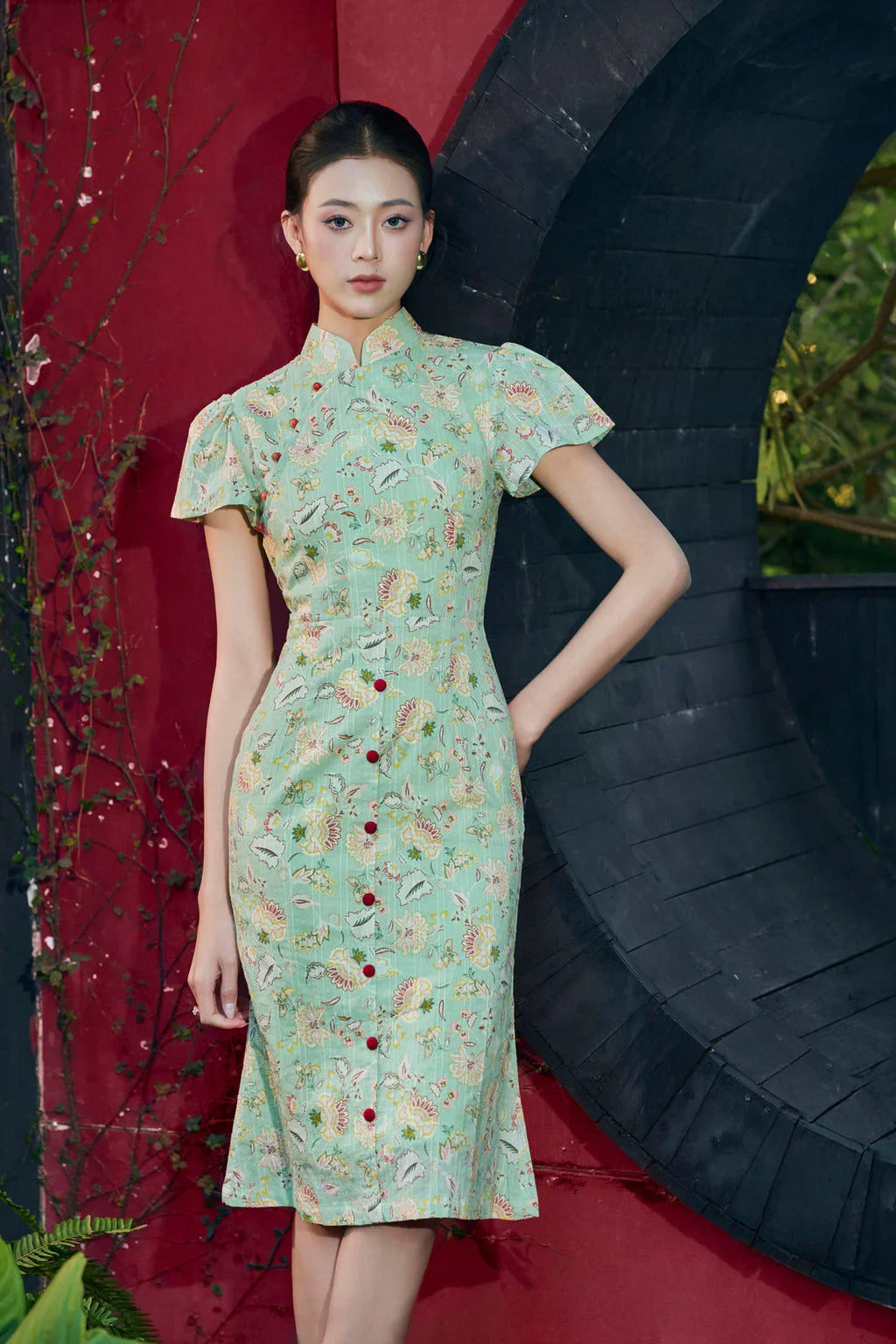 Woman in green floral modern cheongsam dress with mandarin collar and cap sleeves, outdoor setting