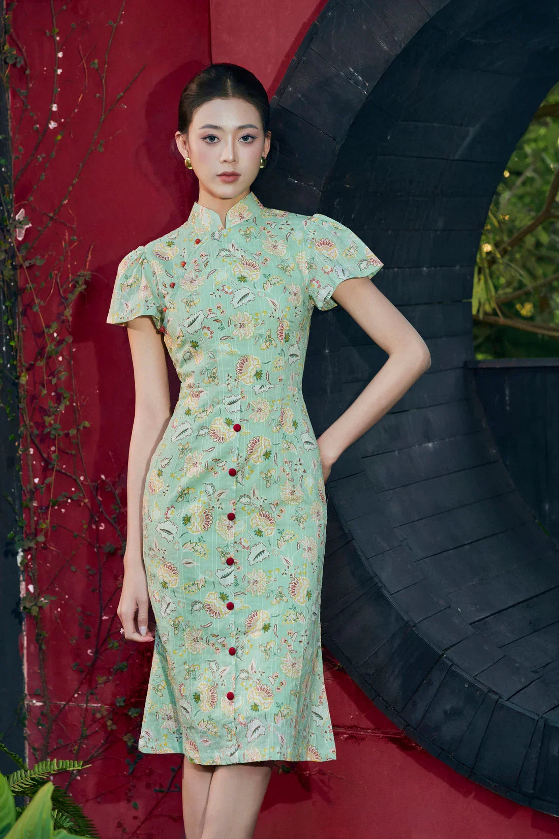 Woman in green floral modern cheongsam dress with mandarin collar and cap sleeves, outdoor setting