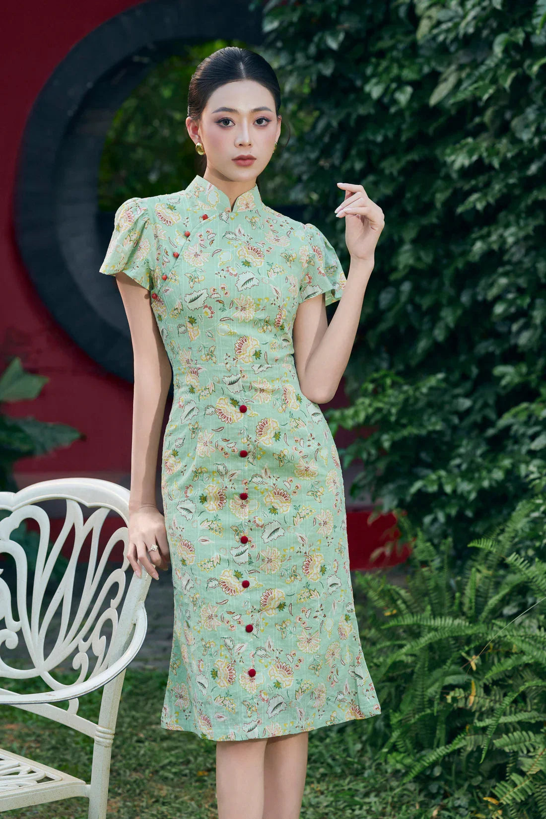 Woman wearing a mint green floral cheongsam dress with cap sleeves, standing outdoors