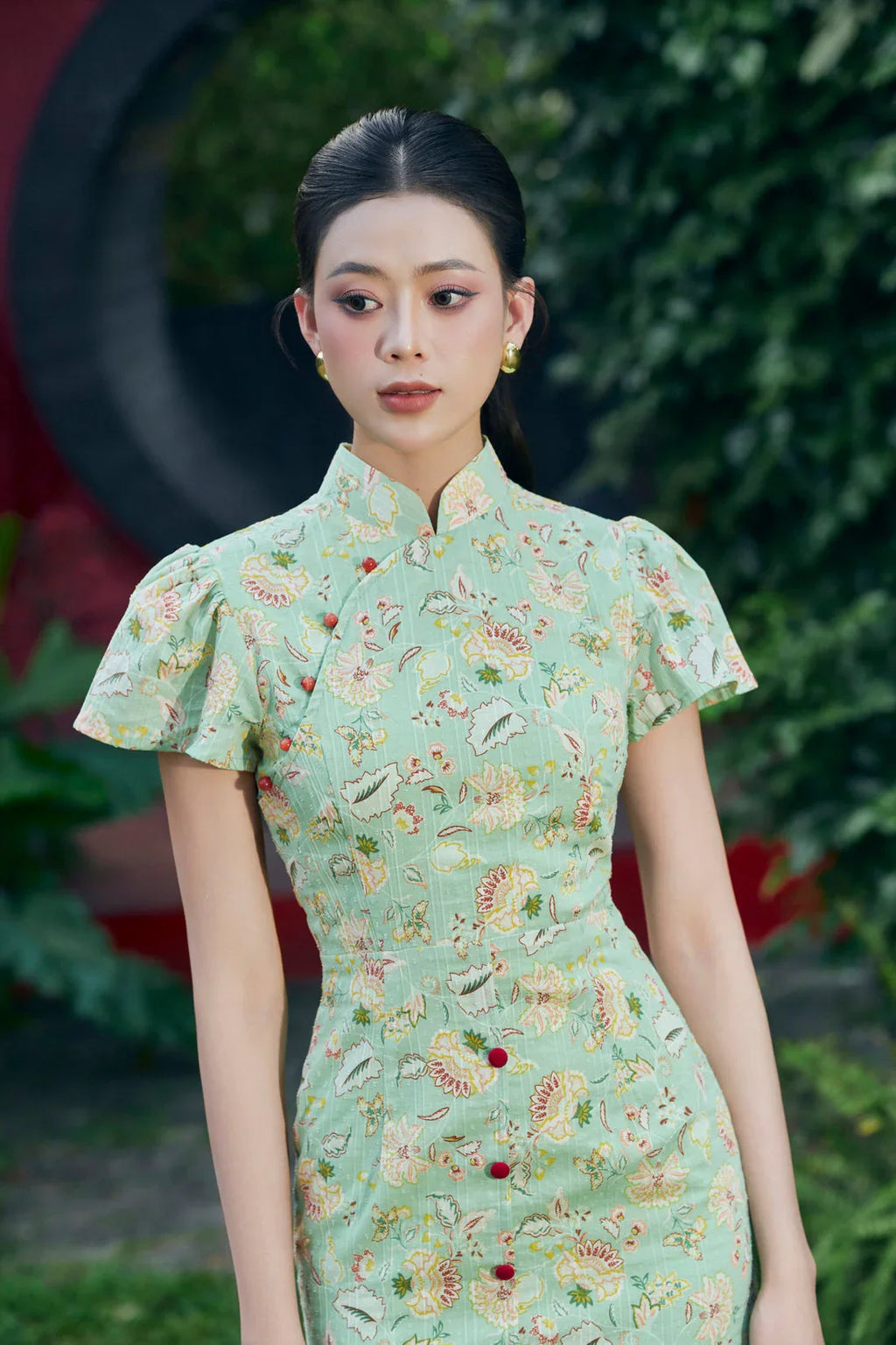 Woman in a mint green modern cheongsam with floral pattern and cap sleeves, outdoor setting