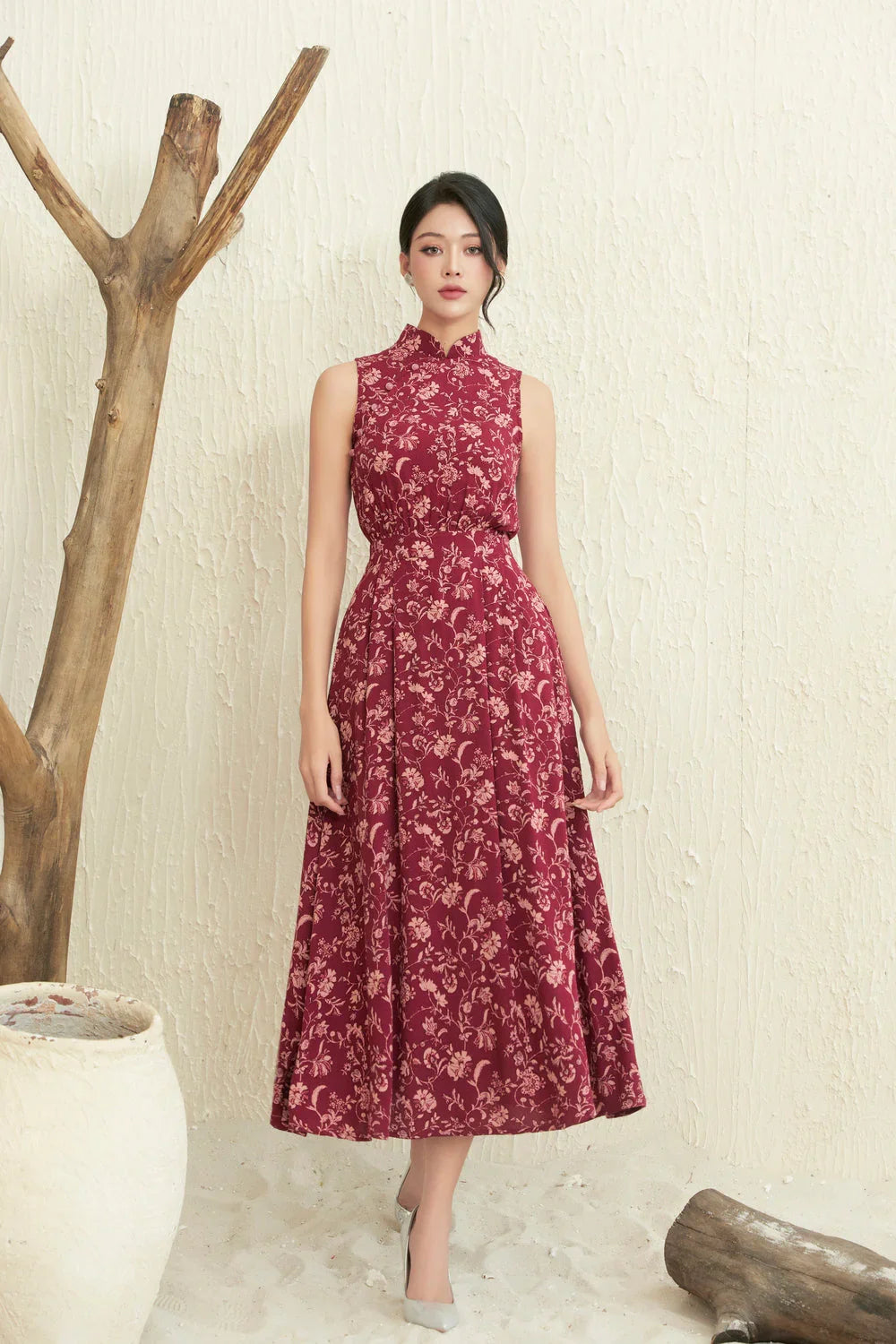 Woman wearing sleeveless maroon floral cheongsam dress with high collar, standing indoors