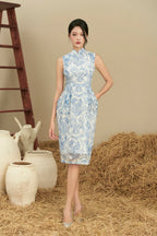 Woman in sleeveless blue and white cheongsam dress with floral pattern, standing on straw