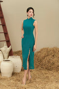 Woman in teal sleeveless modern cheongsam dress with side slit, standing indoors on hay