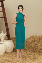 Woman in teal modern cheongsam dress with mandarin collar, standing on straw beside vases