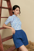 Woman in blue floral modern cheongsam top and blue shorts, leaning on wooden ladder