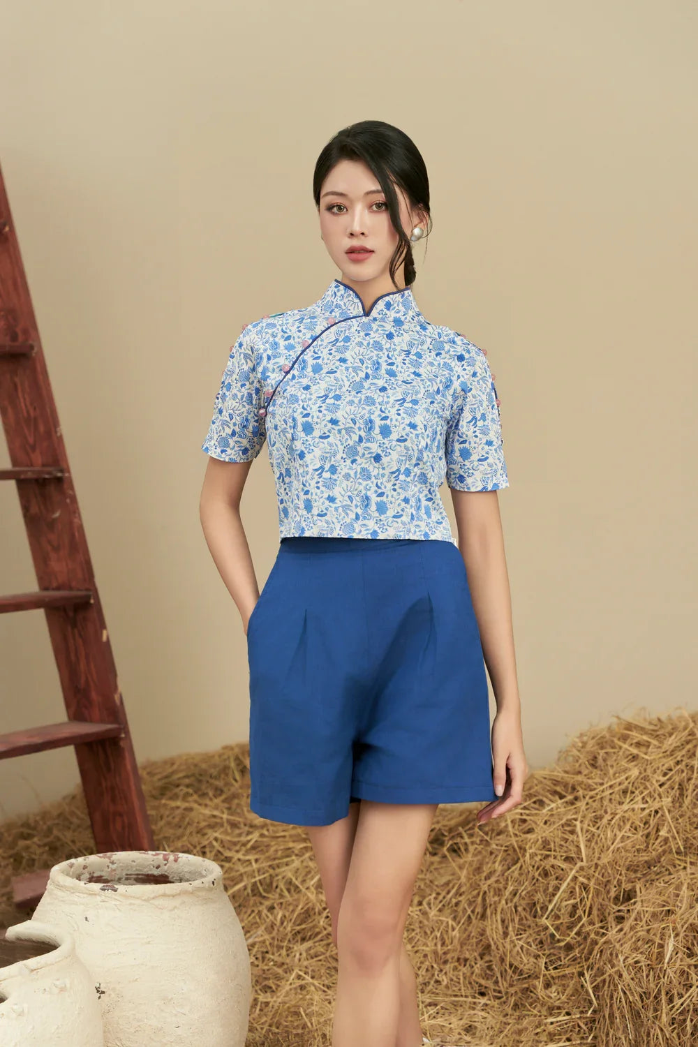 Woman wearing modern blue floral cheongsam top with blue high-waisted shorts, rustic background