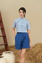 Woman wearing modern blue floral cheongsam top with blue high-waisted shorts, rustic background