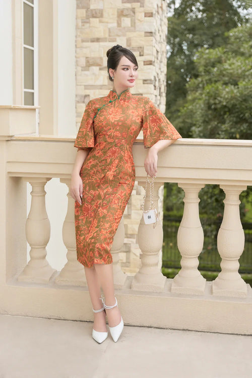 Woman in elegant orange floral cheongsam dress with flared sleeves, standing on balcony