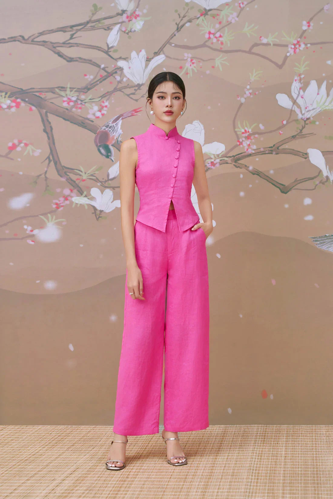 Woman wearing a modern pink cheongsam-inspired sleeveless top and matching wide-leg pants.