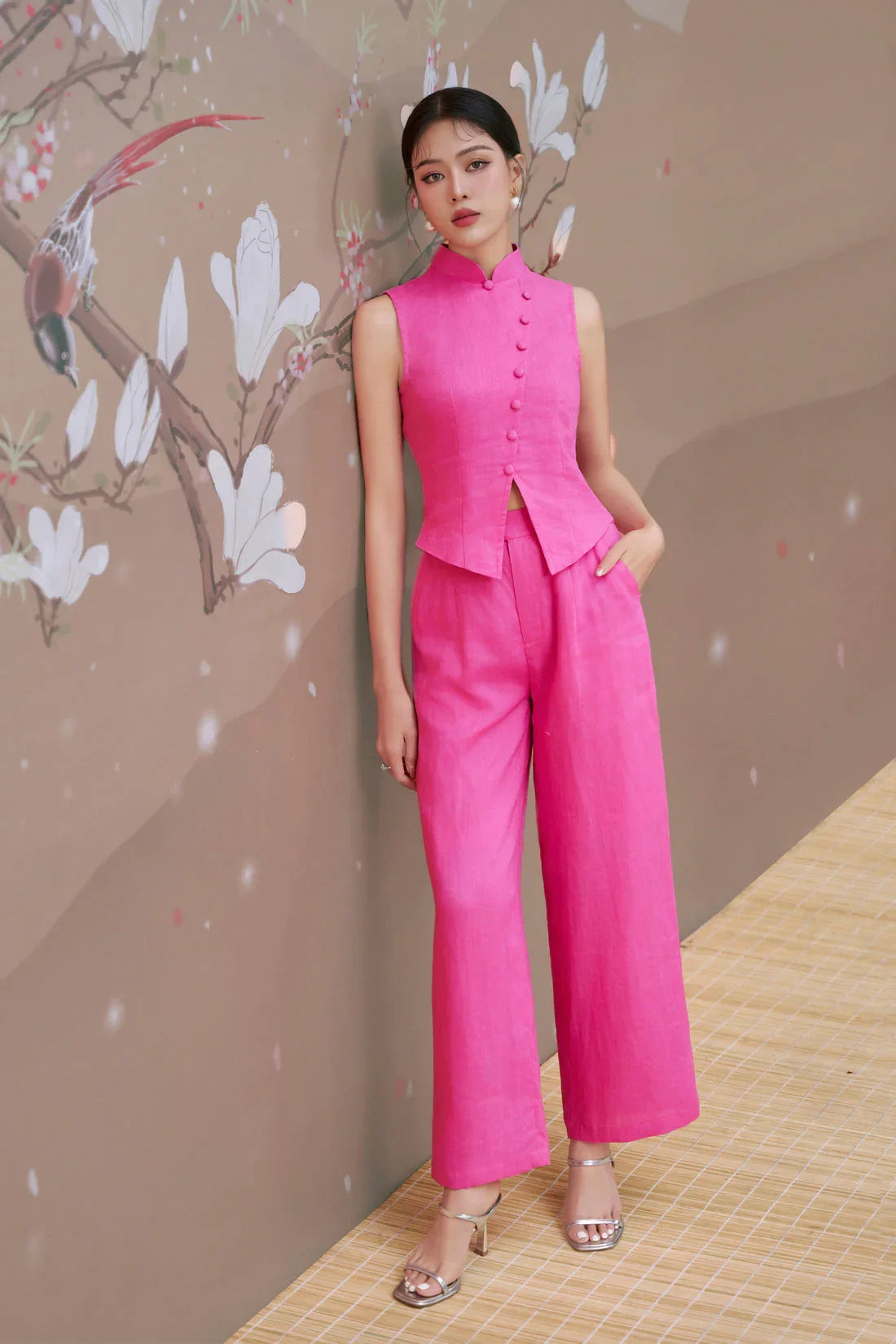 Woman in a sleeveless hot pink modern cheongsam pantsuit, standing by floral mural wall