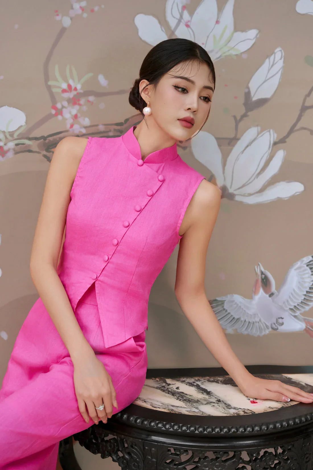 Woman in a modern hot pink sleeveless cheongsam with mandarin collar, floral background