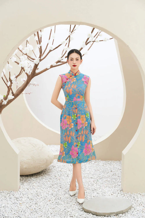 Woman in modern blue floral cheongsam dress, standing in minimalist setting with white blossom branches