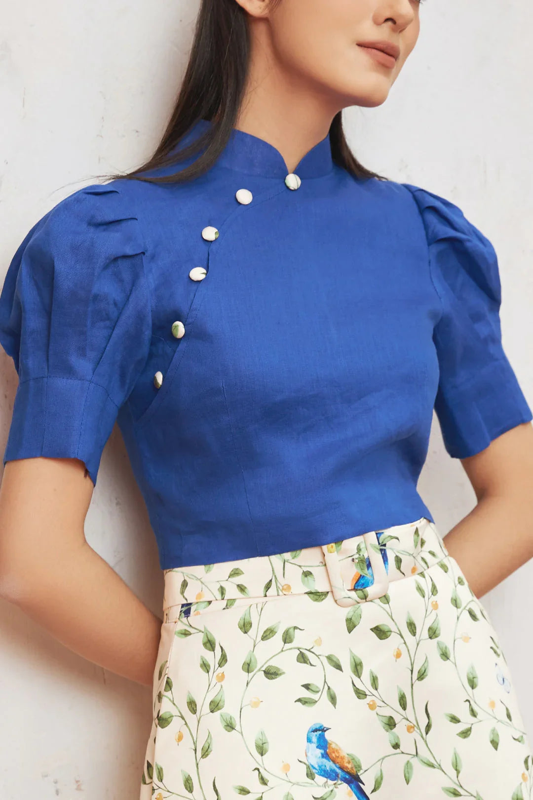Woman wearing modern blue cheongsam top with decorative buttons and floral bird print skirt